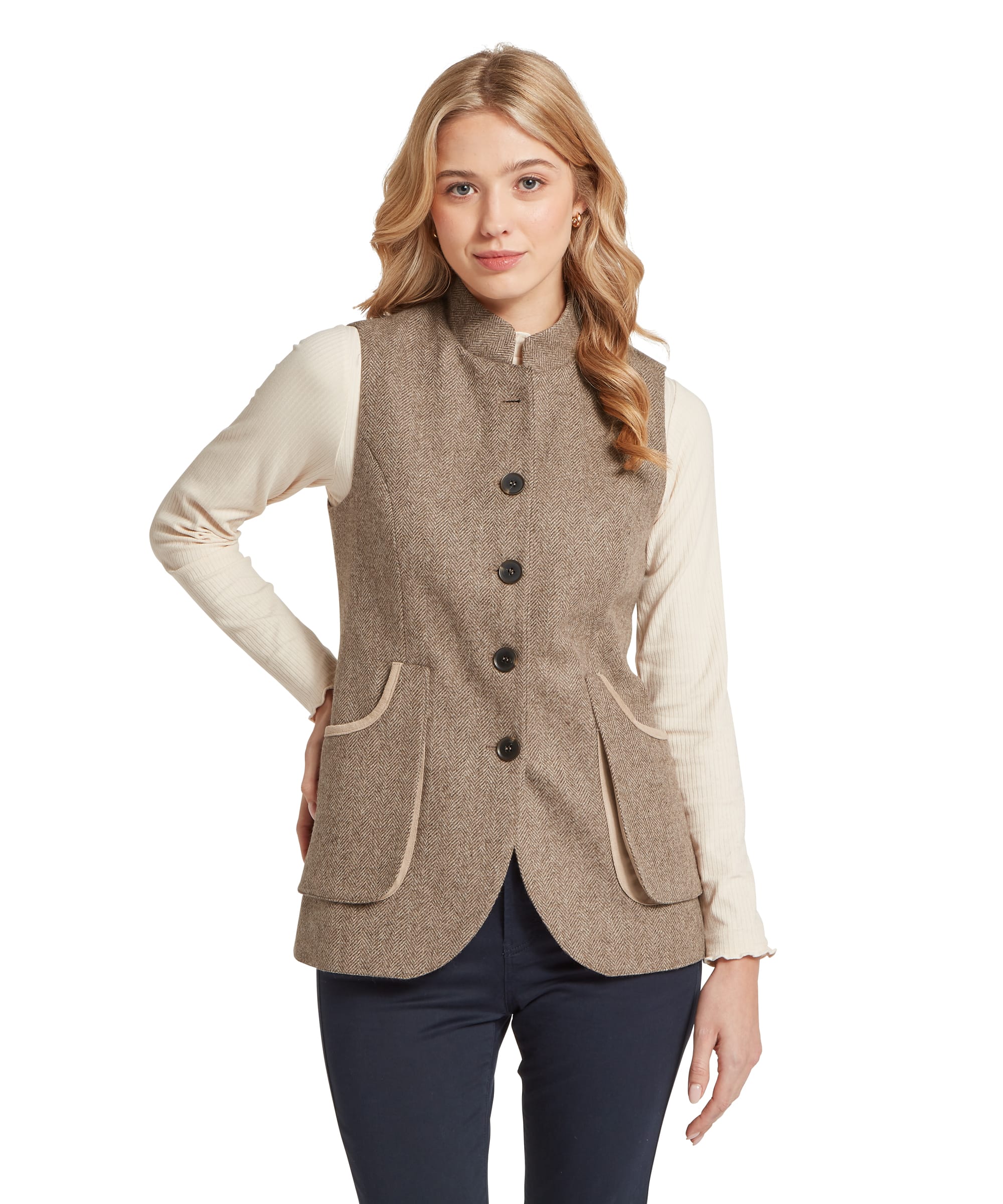 Front view of a woman wearing the Schöffel Women's Pennan Tweed Nehru Waistcoat in Natural Herringbone, showing the fitted silhouette, single-breasted button fastening, contrast cream pocket trim and patch pockets, layered over a cream ribbed polo neck top and navy trousers