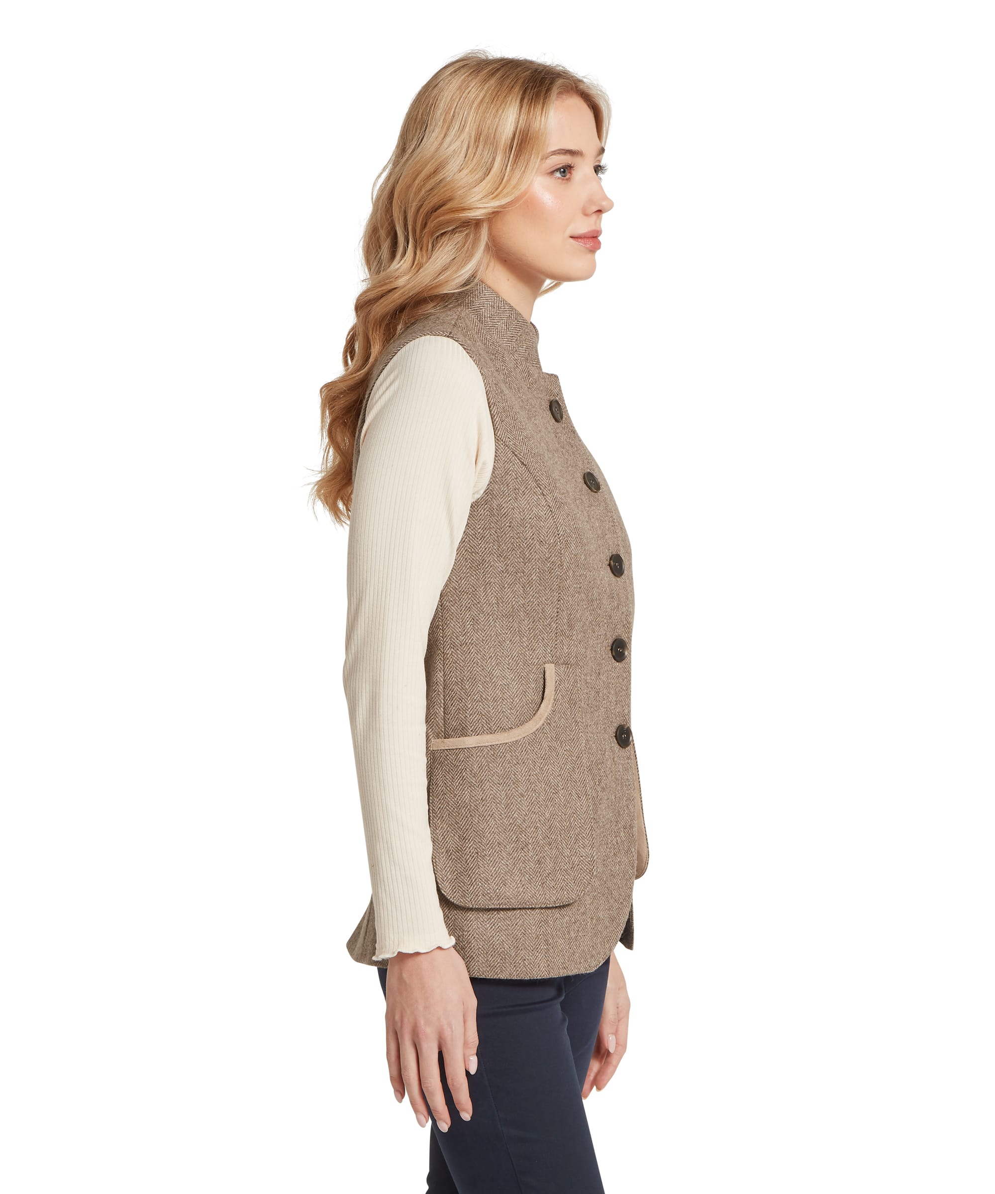 Schöffel Women's Pennan Tweed Waistcoat in grey herringbone tweed, side view showing single-breasted button fastening, suede-trim patch pockets, fitted silhouette, and herringbone weave texture, worn over a cream ribbed long-sleeve top with navy trousers