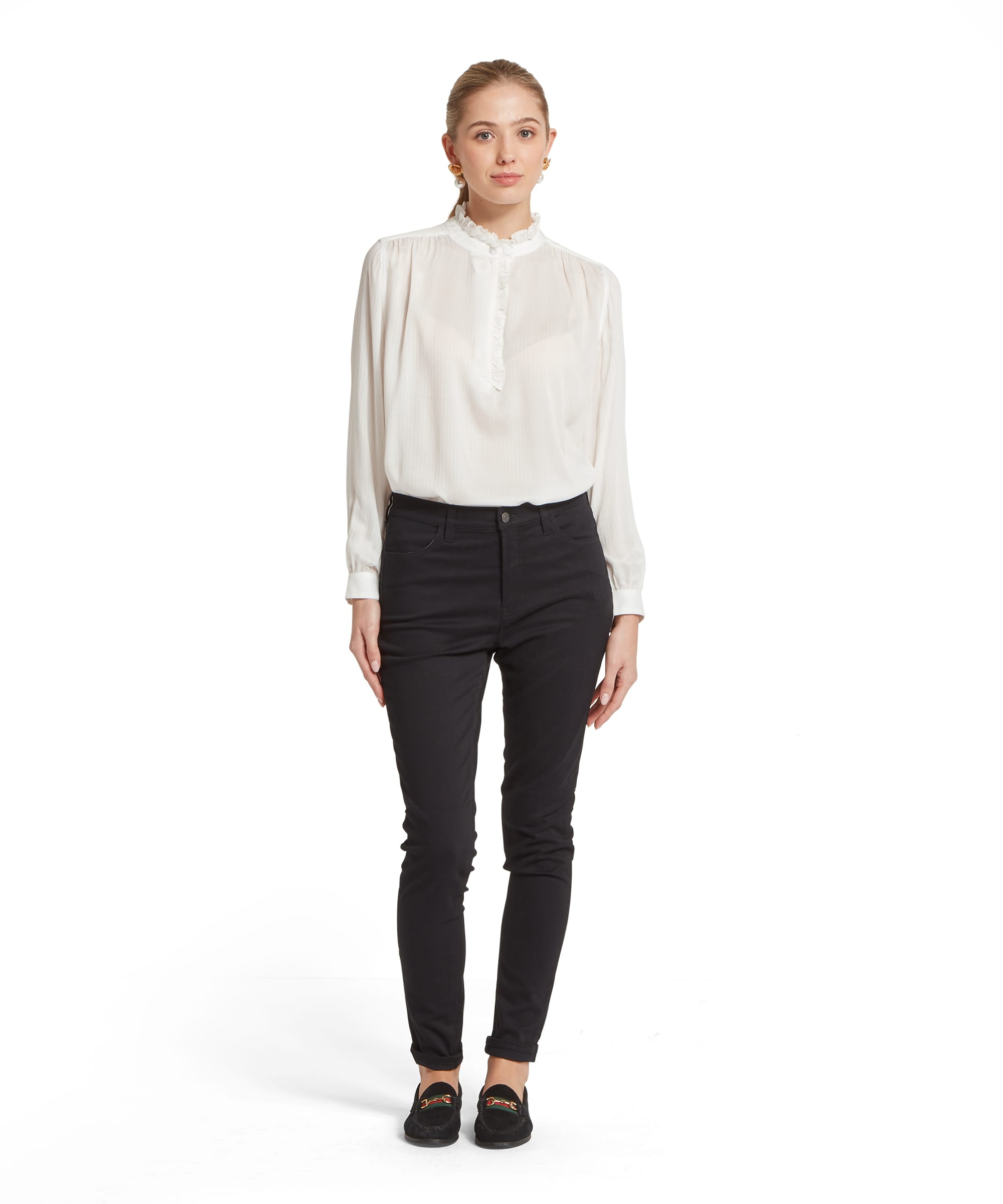 Woman wearing black high-waisted poppy jeans paired with a white long-sleeved blouse with a ruffled