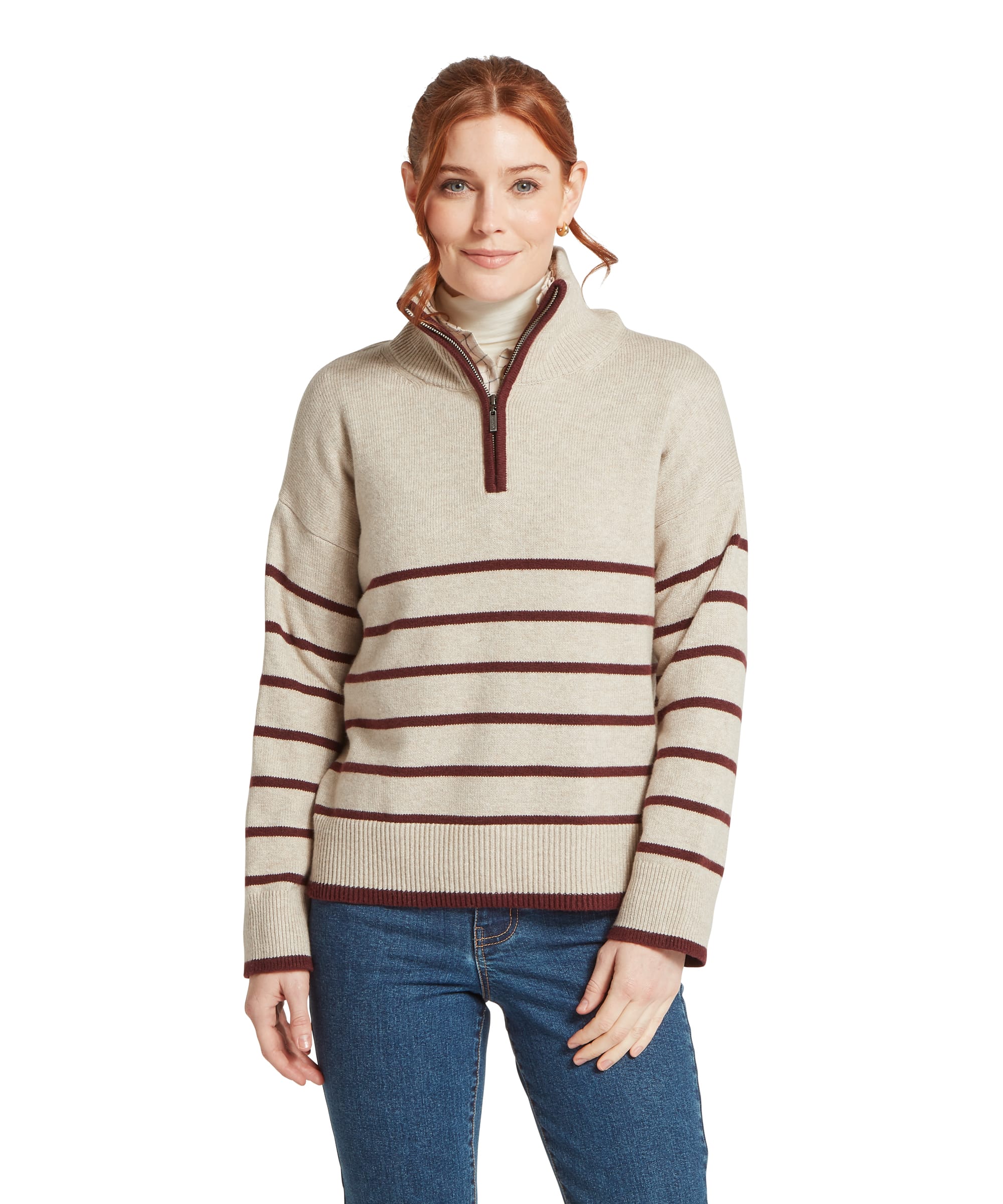Front view of a woman wearing the Schöffel Women's Sandsend 1/4 Zip Knit Jumper in Oatmeal with contrast burgundy stripe, featuring a relaxed fit, ribbed hem and contrast zip trim, layered over a cream roll neck top and blue jeans