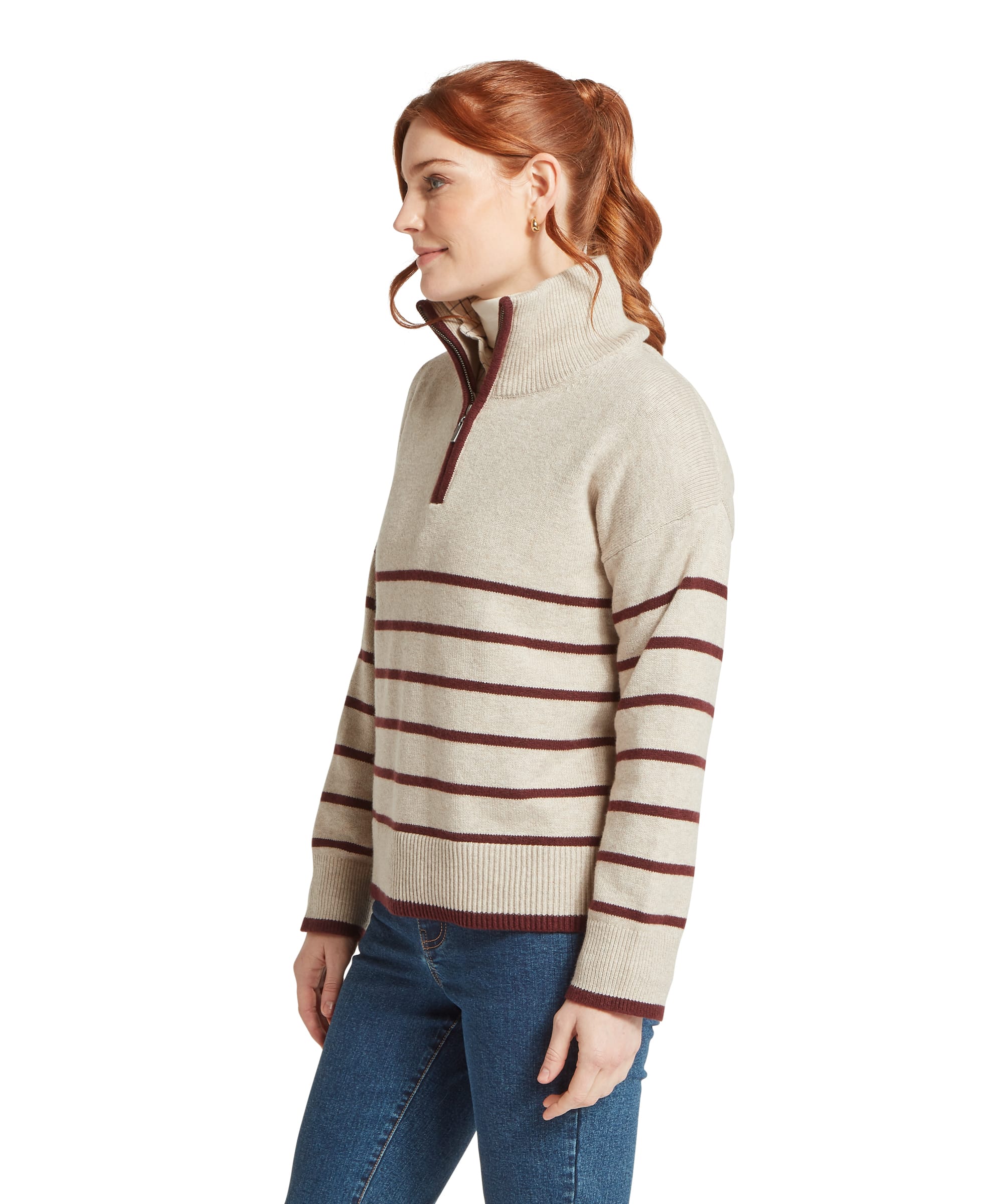 Side profile of the Schöffel Women's Sandsend 1/4 Zip Knit Jumper in Oatmeal with burgundy stripe, highlighting the oversized silhouette, contrast quarter-zip trim and ribbed cuffs, worn over a cream base layer and blue jeans