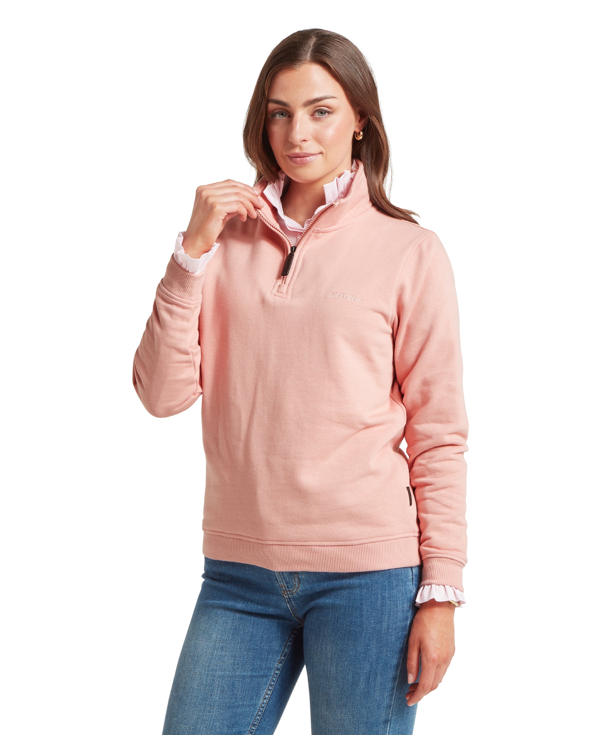 Woman wearing a light pink quarter-zip sweatshirt with ribbed hem and cuffs, layered over a white ruffled-cuff shirt. Paired with blue jeans. A small embroidered Schöffel logo is visible on the left chest. Holding the collar with one hand, slightly pulling it up. Standing front-facing against a plain white background.