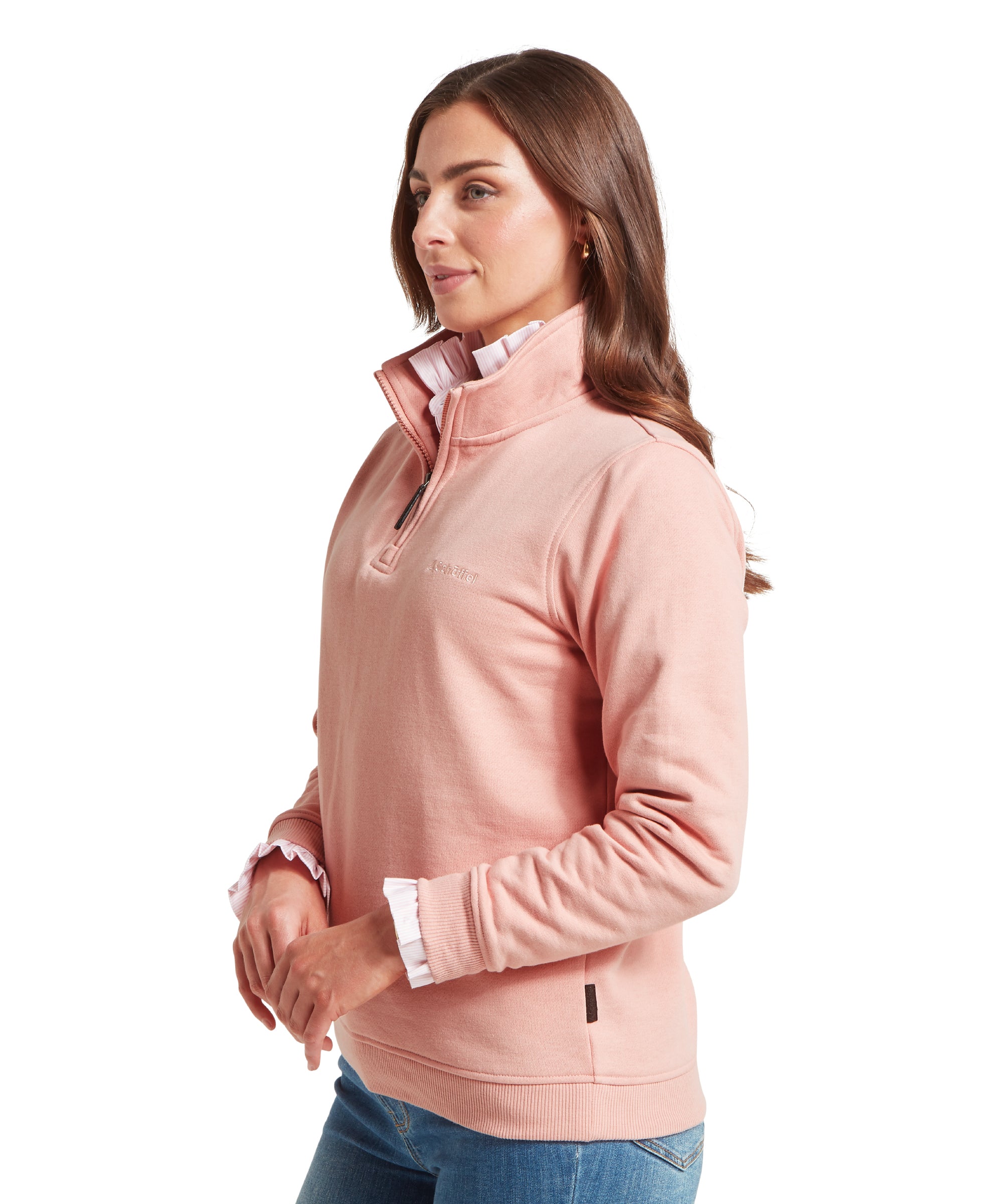 Woman wearing a light pink quarter-zip sweatshirt with a high collar and visible zip. Layered over a white shirt with ruffled cuffs at the collar and wrists. Paired with blue jeans. Subtle Schöffel branding embroidered on the chest and a small tag near the hem. Standing front-facing against a plain white background.