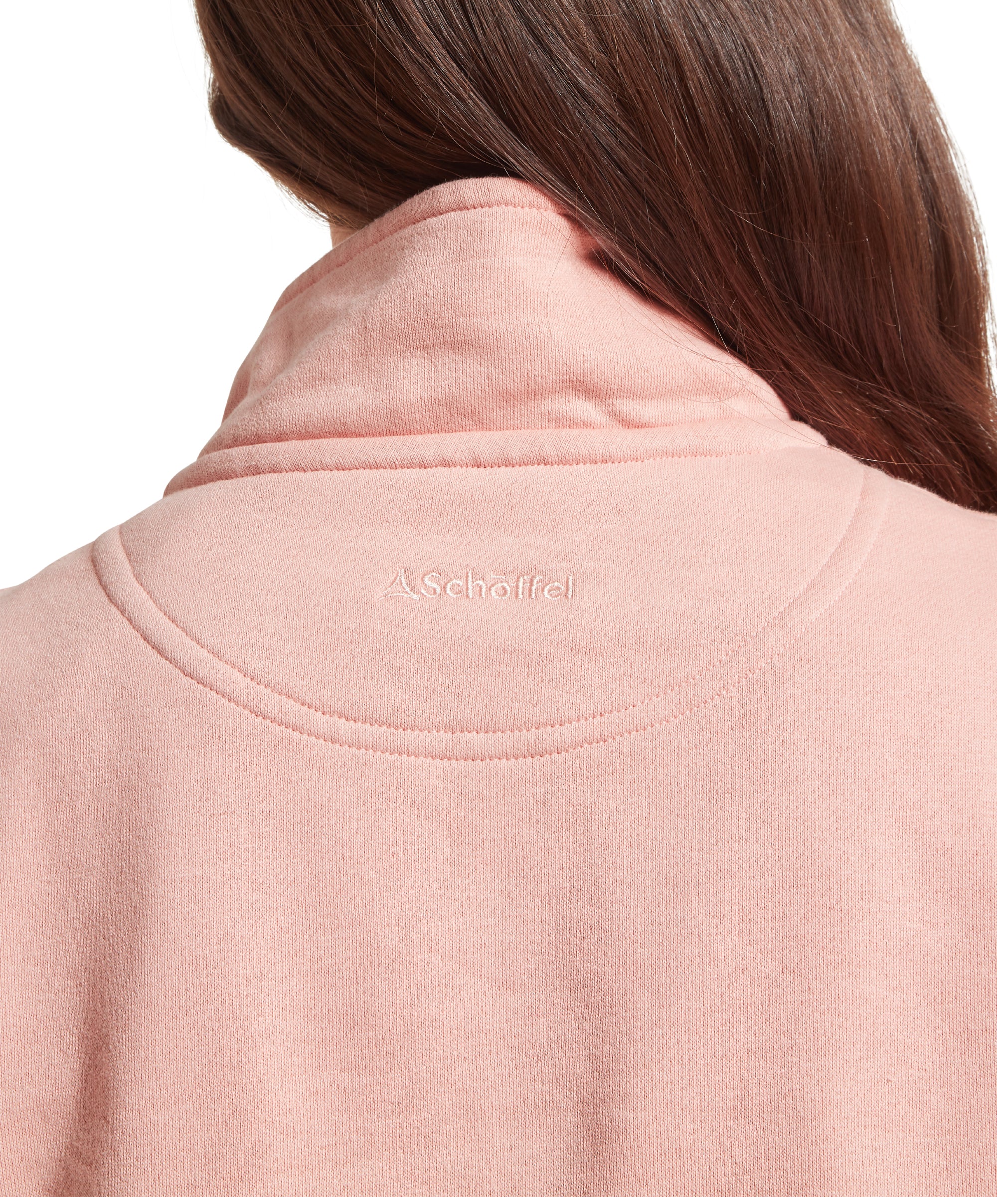 Back view of a woman wearing a light pink  sweatshirt with a high collar and textured, wavy pattern. “Schöffel” and logo embroidered in white on the upper back below the collar. Long brown hair cascading over the right shoulder. Standing upright against a plain white background.