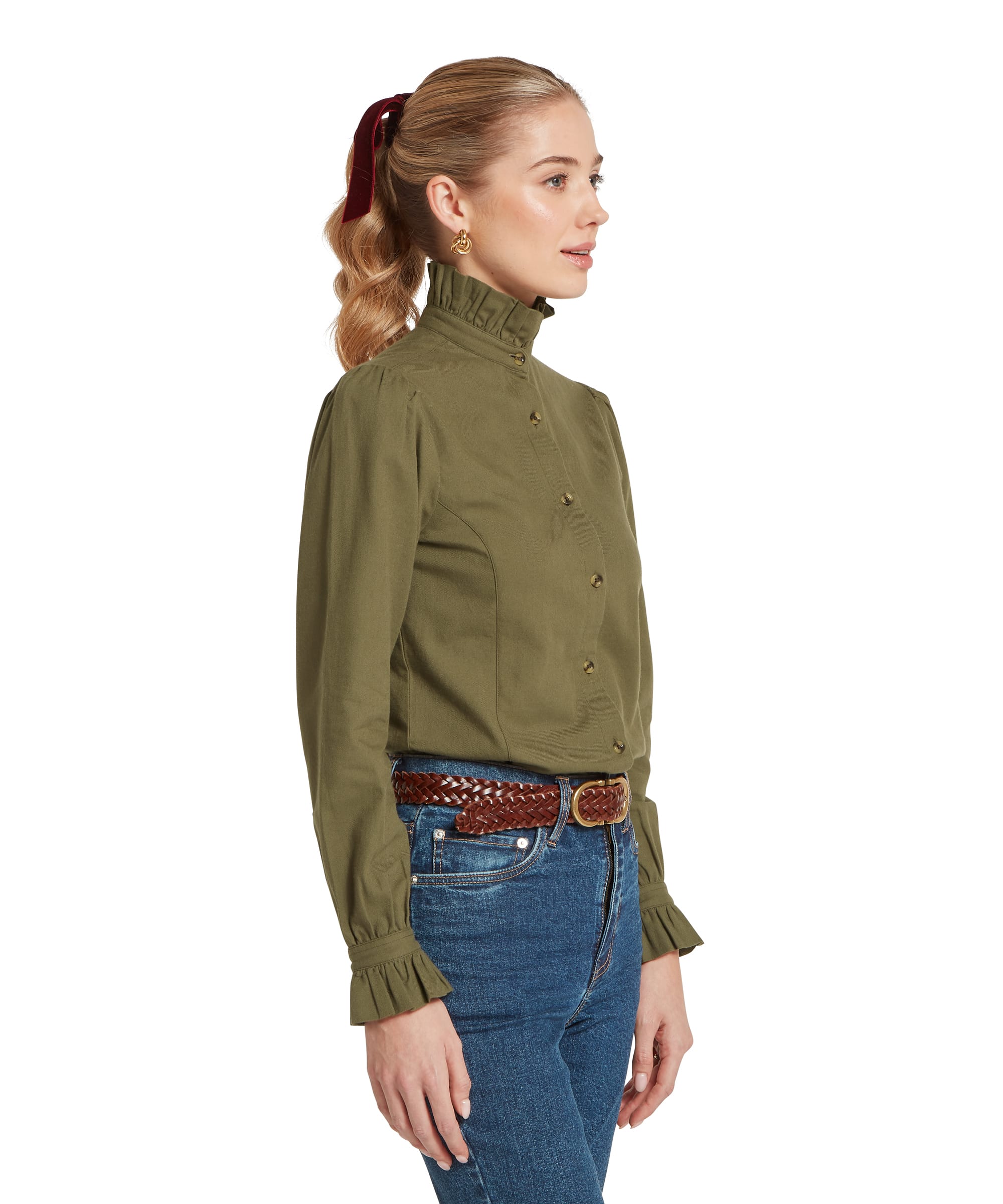 Side profile of the Schöffel Women's Sheringham Shirt in Khaki Green, highlighting the structured puff sleeve, fitted bodice and antique brass button placket, worn with blue jeans and a tan plaited leather belt