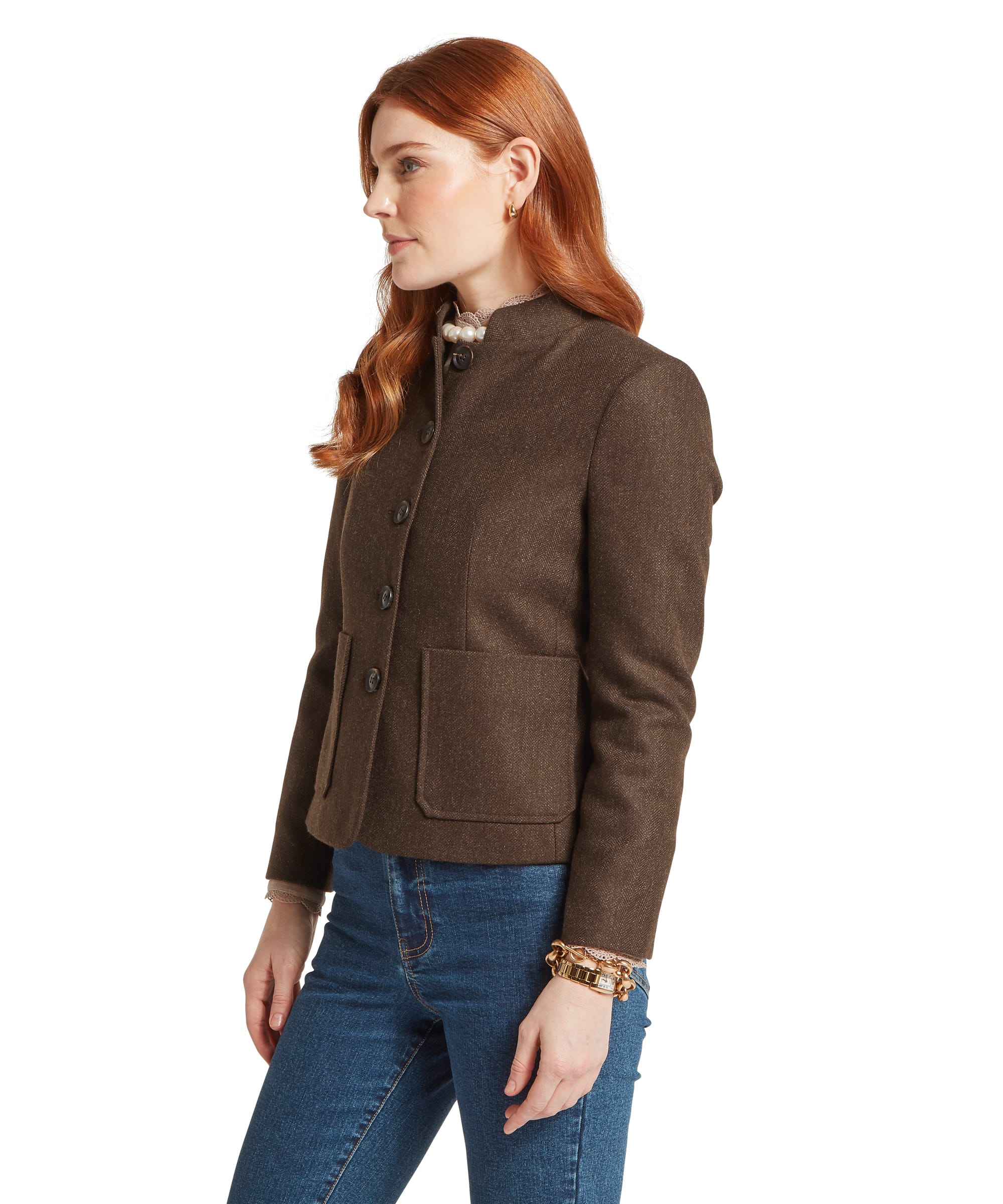 Schöffel Women's St Abbs Tweed Blazer in dark brown herringbone tweed, side view showing the collarless Nehru neckline, dark horn-effect button fastening, patch hip pockets, and tailored fit, styled with blue jeans and a camel lace blouse with pearl collar pin