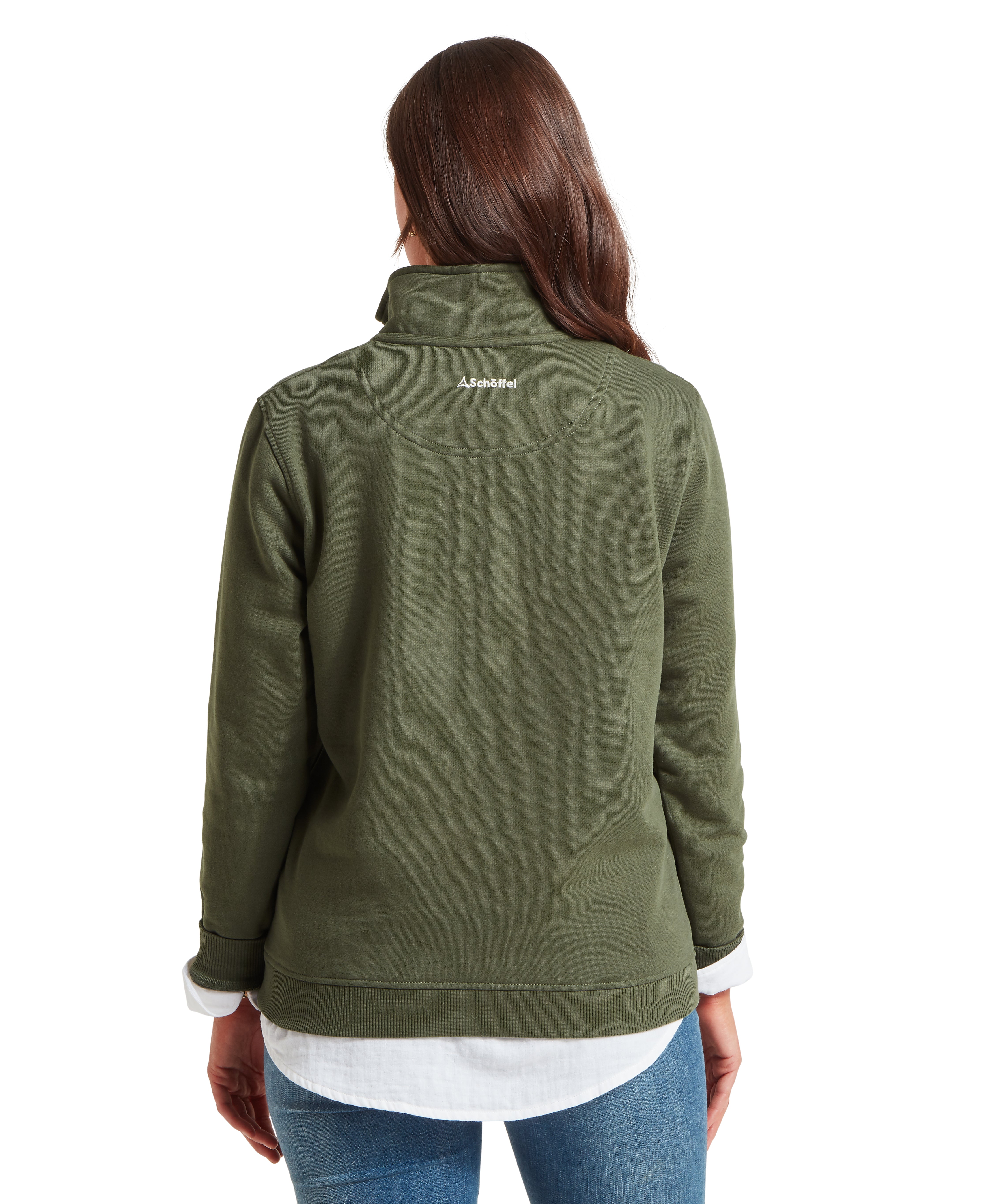 Rear view of a woman with long brown hair wearing a green sweatshirt. The garment features a curved yoke seam across the upper back with a small white Schöffel logo centered below the collar. A white shirt extends past the bottom hem of the fleece.