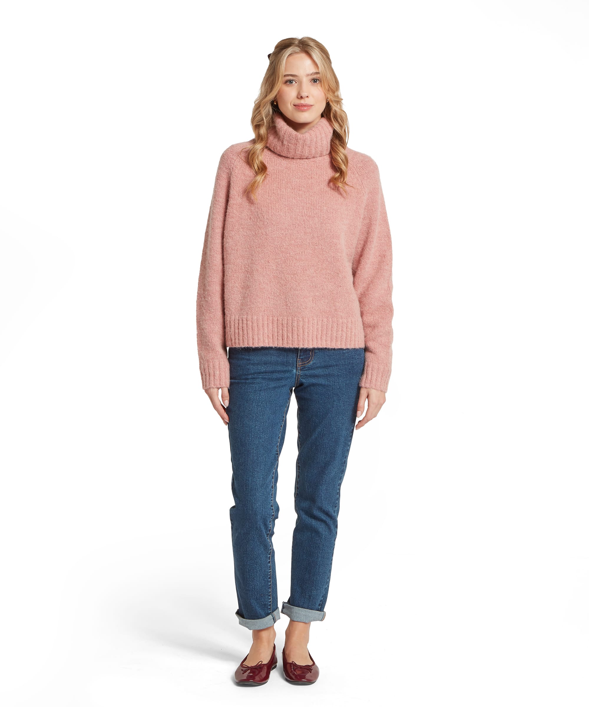Full-length front view of the Schöffel Women's Sutton Roll Neck Jumper in Blush Pink, showing the relaxed oversized silhouette, chunky knit texture, deep roll neck and ribbed cuffs and hem, worn with turn-up blue jeans and burgundy ballet flats