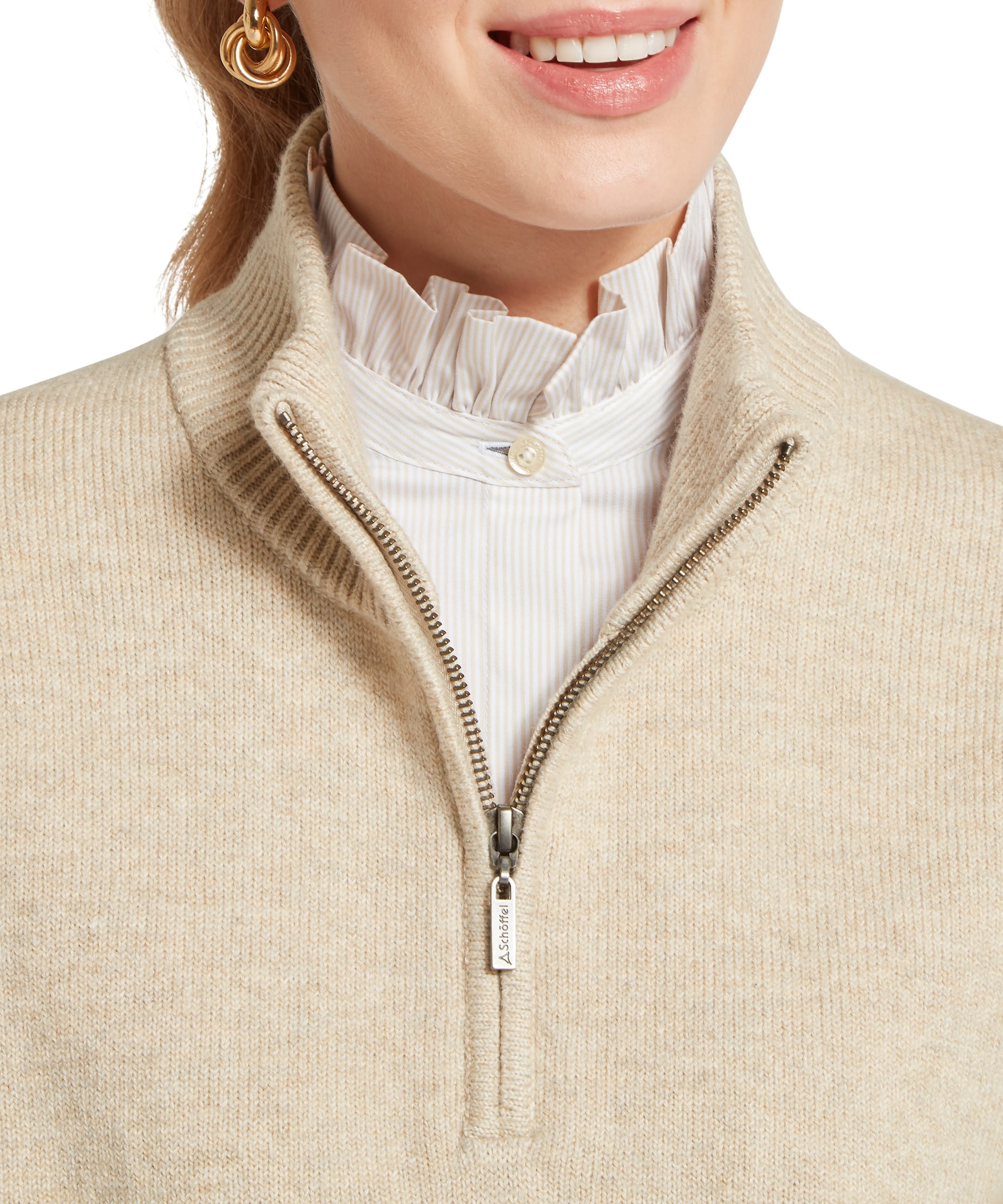 Close-up detail of the Women's Schöffel Thoralby Quarter-Zip Jumper in oatmeal cream, showing the antique brass Schöffel branded zip pull, ribbed funnel neck and layered country styling over a striped frill-collar shirt.