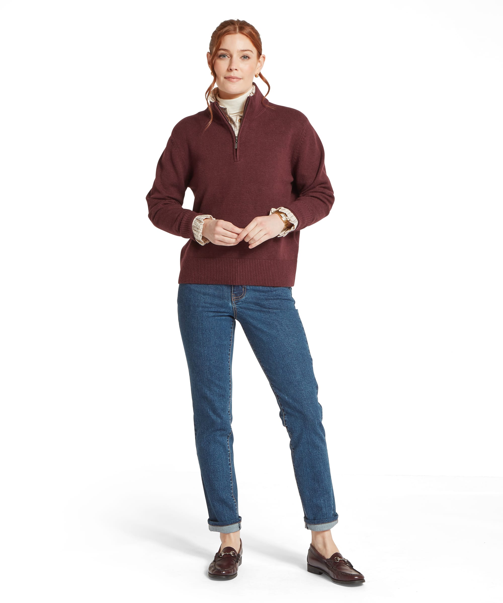 Full-length view of the Women's Schöffel Thoralby Quarter-Zip Jumper in burgundy, an oversized warm knit with ribbed cuffs and hem, layered over a cream check shirt with relaxed-fit blue denim jeans with turn-ups and dark horsebit loafers.