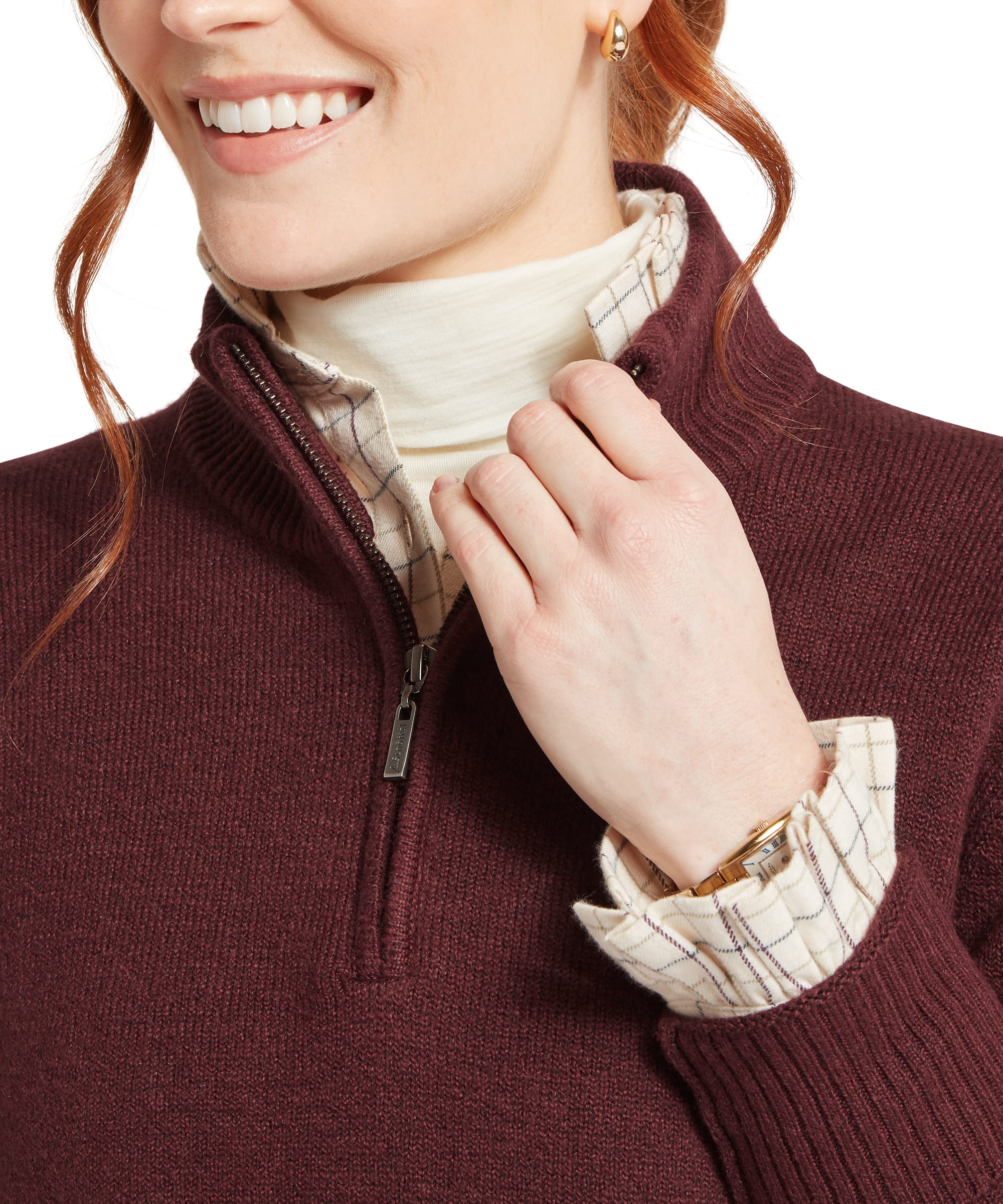 Close-up detail of the Women's Schöffel Thoralby Quarter-Zip Jumper in rich burgundy, highlighting the Schöffel branded zip pull, ribbed stand collar and warm knit fabric, layered over a cream check shirt collar, accessorised with a gold watch.