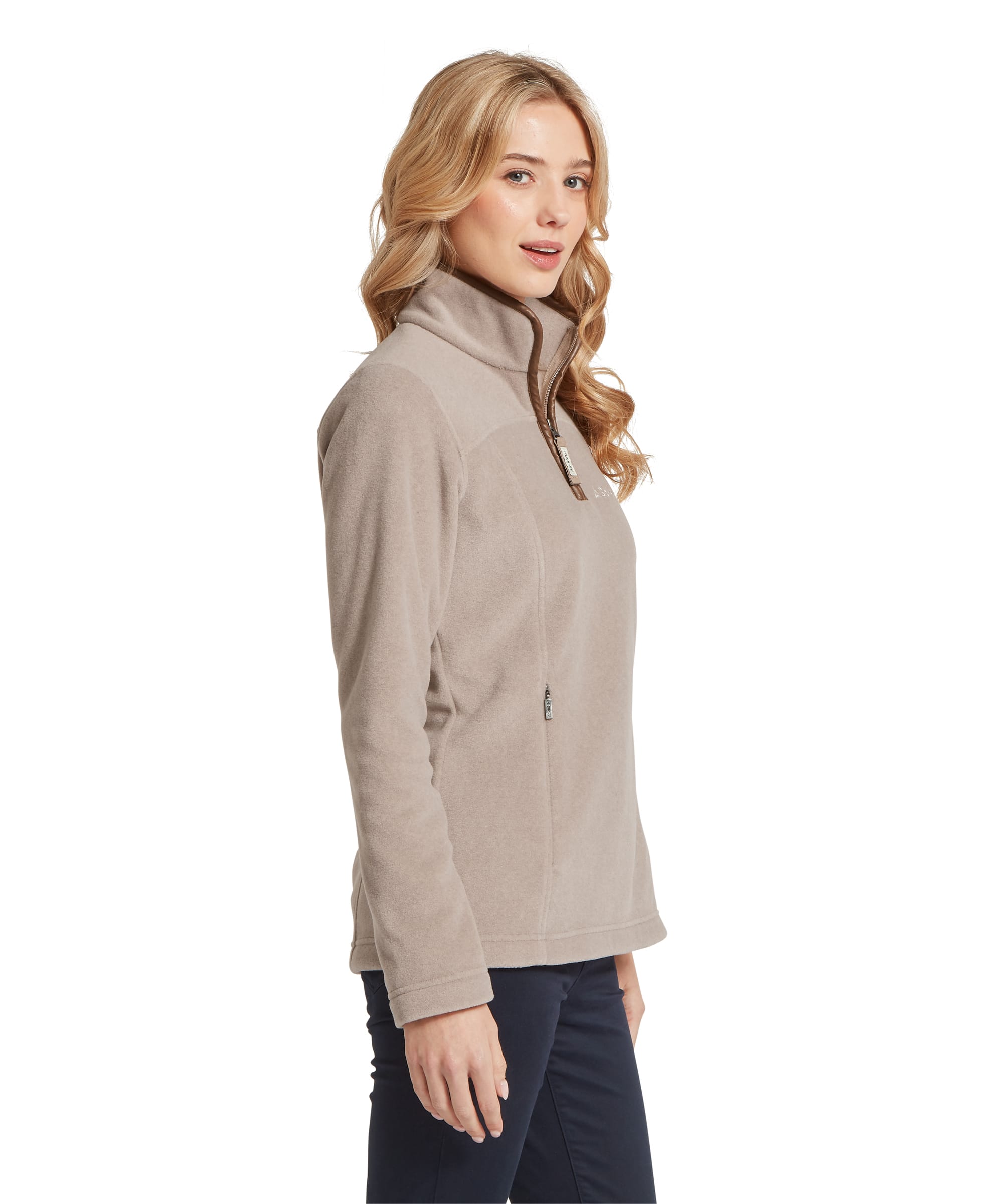 Side view of the Women's Schöffel Tilton II Quarter-Zip Fleece in stone beige, showing the contrast brown zip trim at the collar, Schöffel branded zip pull on the side pocket and the fleece's fitted shaping with side seam panels, styled with navy trousers.