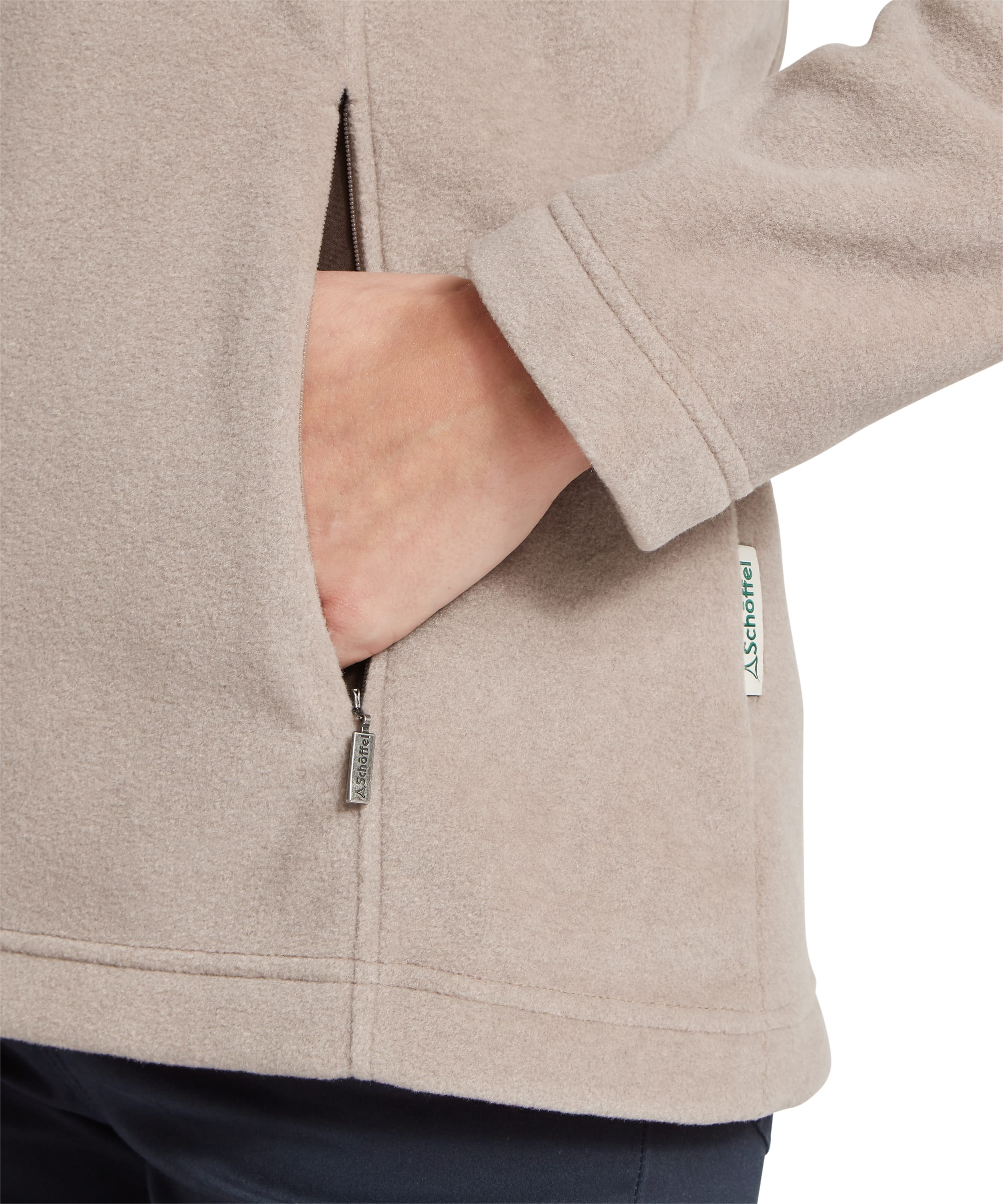 Close-up detail of the side pocket on the Women's Schöffel Tilton II Quarter-Zip Fleece in stone beige, showing the Schöffel branded zip pull, woven label and the soft micro-fleece texture with hand in the open pocket.