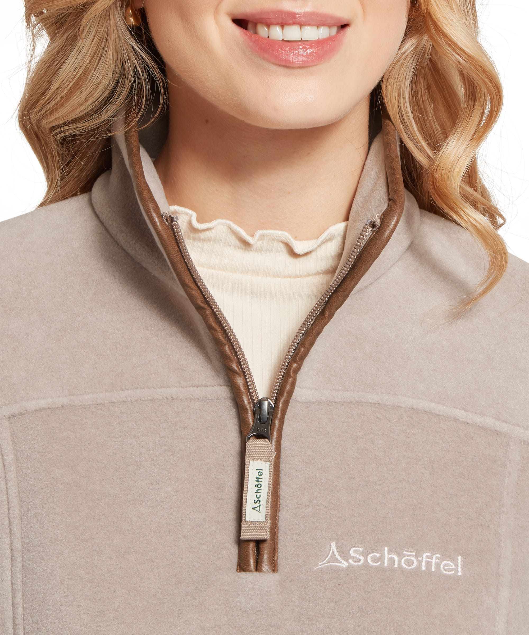 Close-up of the quarter-zip collar on the Schöffel Women's Tilton II 1/4 Zip Fleece in Camel, with the Schöffel branded zip pull and contrast leather-look trim, layered over a cream ribbed polo neck top