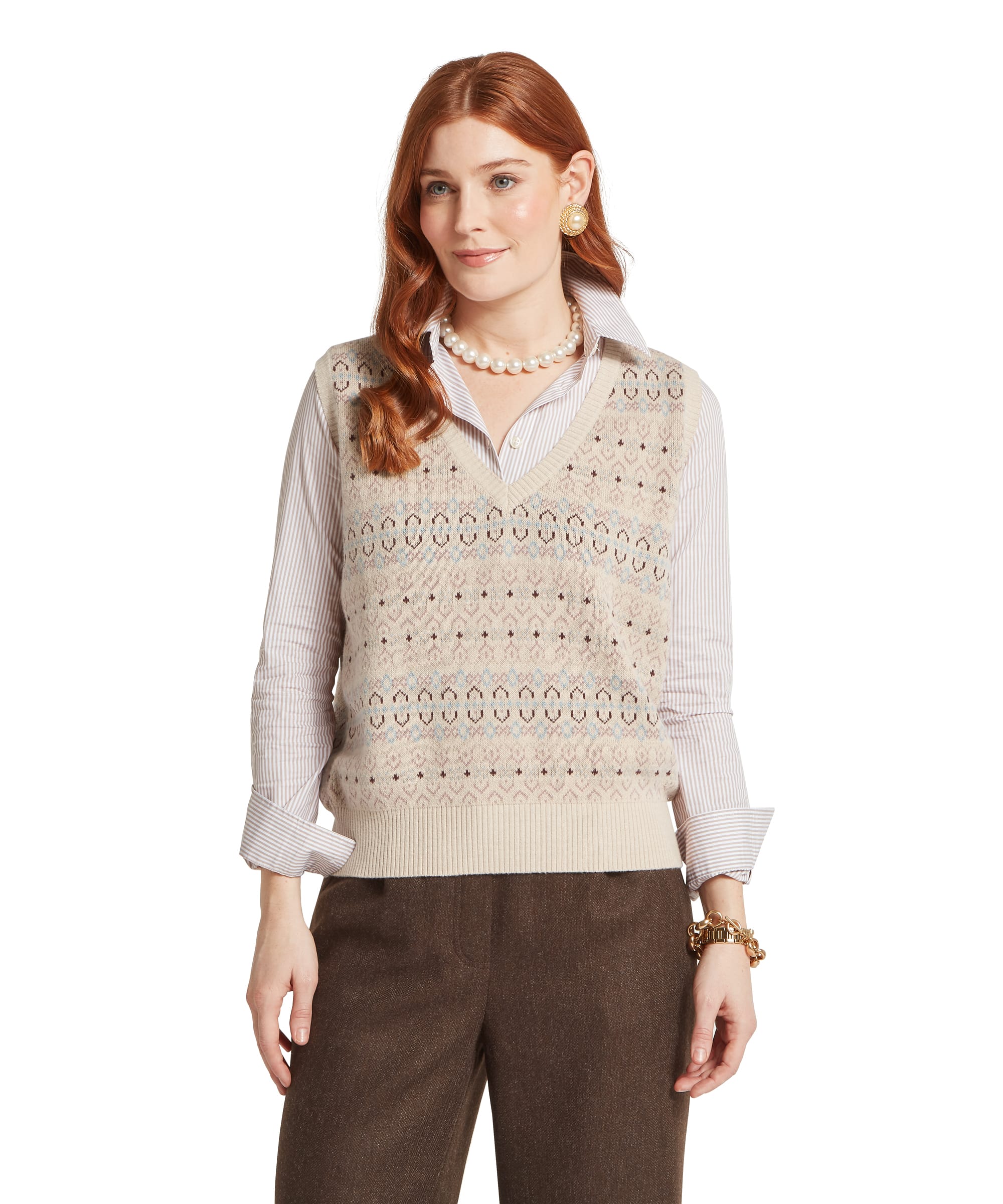 Women's Schöffel Tresness Fair Isle Vest in oatmeal cream, featuring an all-over Fair Isle pattern in dusky pink, cornflower blue and chocolate brown with a V-neckline and ribbed hem, layered over a pink stripe shirt, with brown tweed wide-leg trousers, a pearl necklace and pearl drop earring.